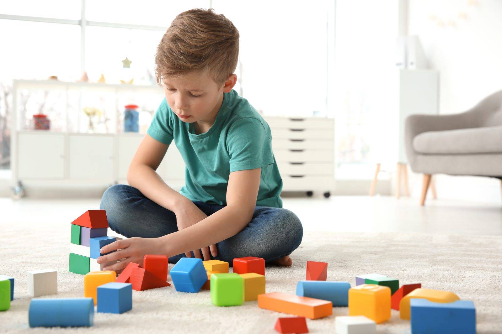 A young boy building with colorful wooden blocks on a living room rug
